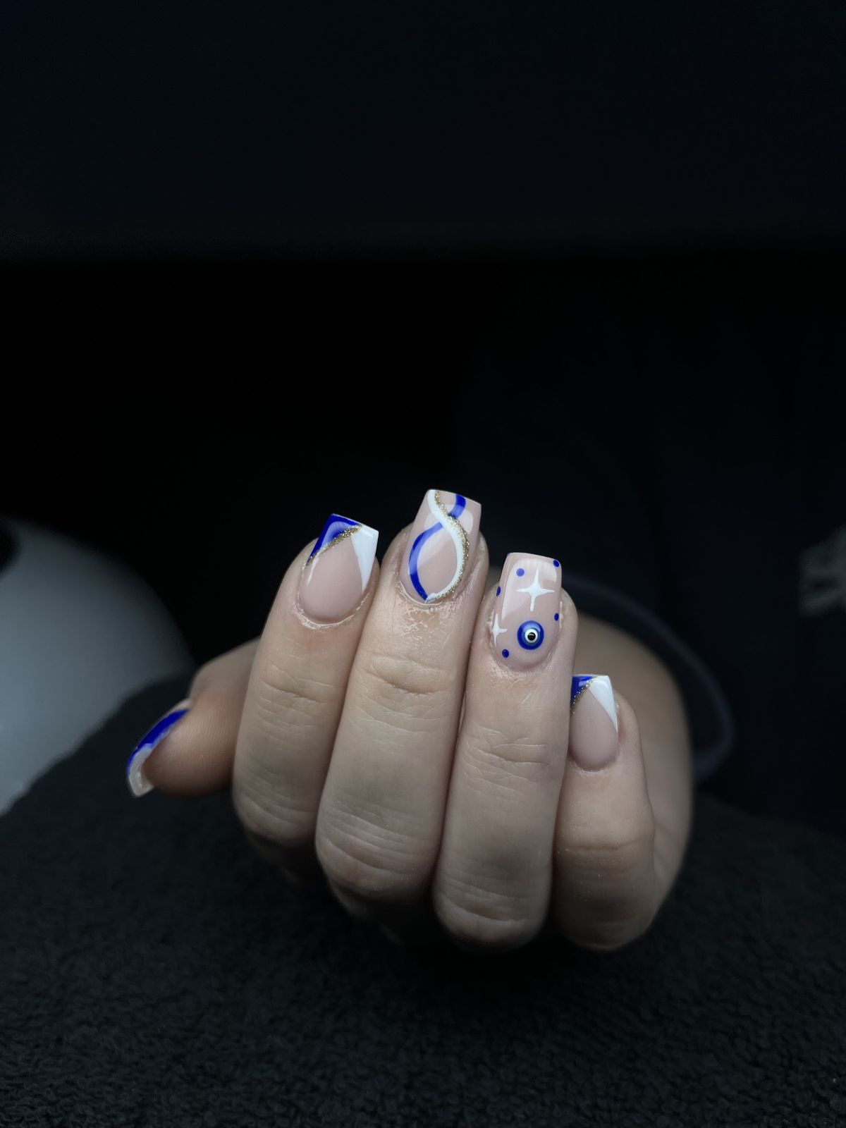 Nude nagels met kobaltblauwe krullende lijnen en een oogje als accent